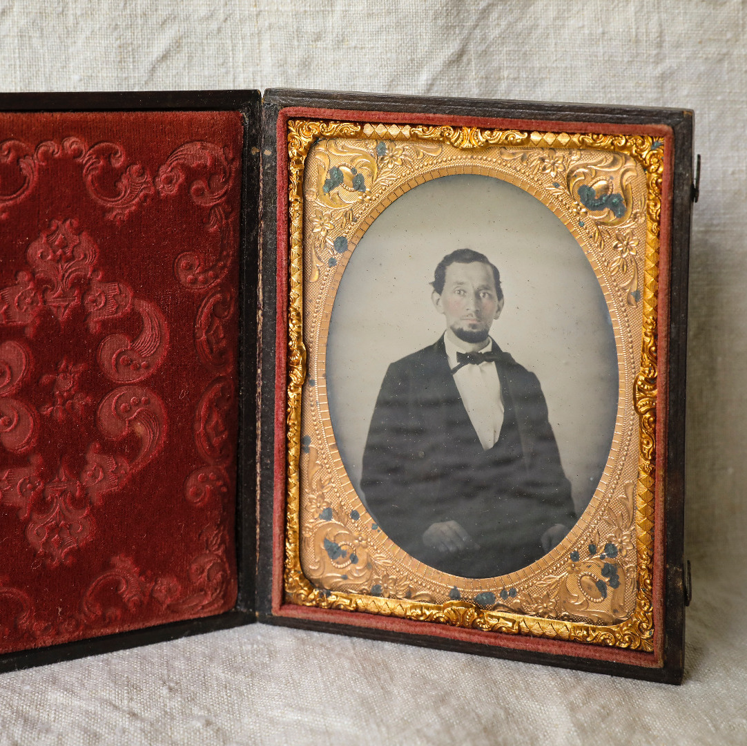 Old black and white photo of a man in a suit inside of a gold frame and a red velvet case